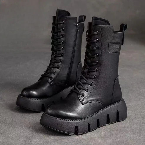 Bottes noires en cuir à plateforme épaisse, lacets et fermeture éclair latérale, posées sur un fond gris. Chaussures tendance, style militaire.