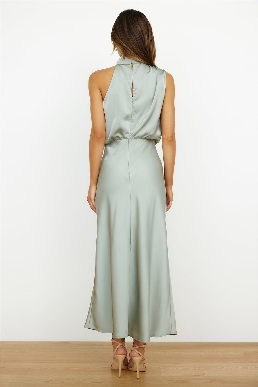 Robe longue en satin vert sauge, sans manches, dos ouvert, portée par une femme de dos, sur fond blanc. Mode élégante, tenue de soirée chic.