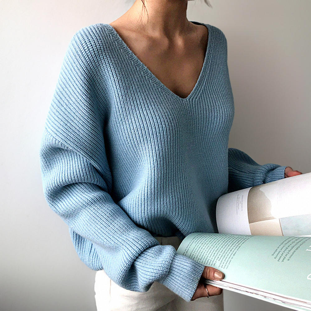 Femme portant un pull bleu en tricot à col en V, lisant un magazine. Mode automne, style décontracté, vêtements confortables.