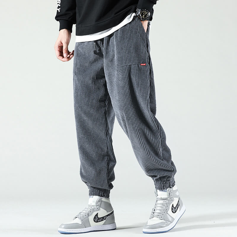 Pantalon jogger gris en velours côtelé pour homme, style décontracté, avec baskets blanches et grises. Mode urbaine tendance.
