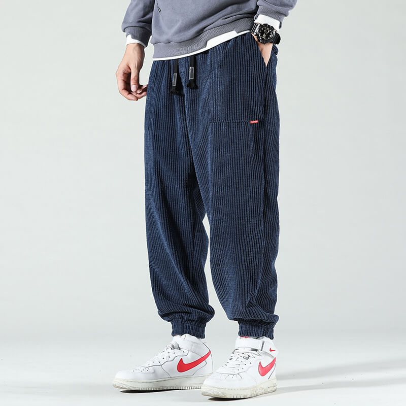 Pantalon jogger bleu côtelé pour homme, style décontracté, avec poches latérales. Porté avec des baskets blanches et un sweat-shirt gris.