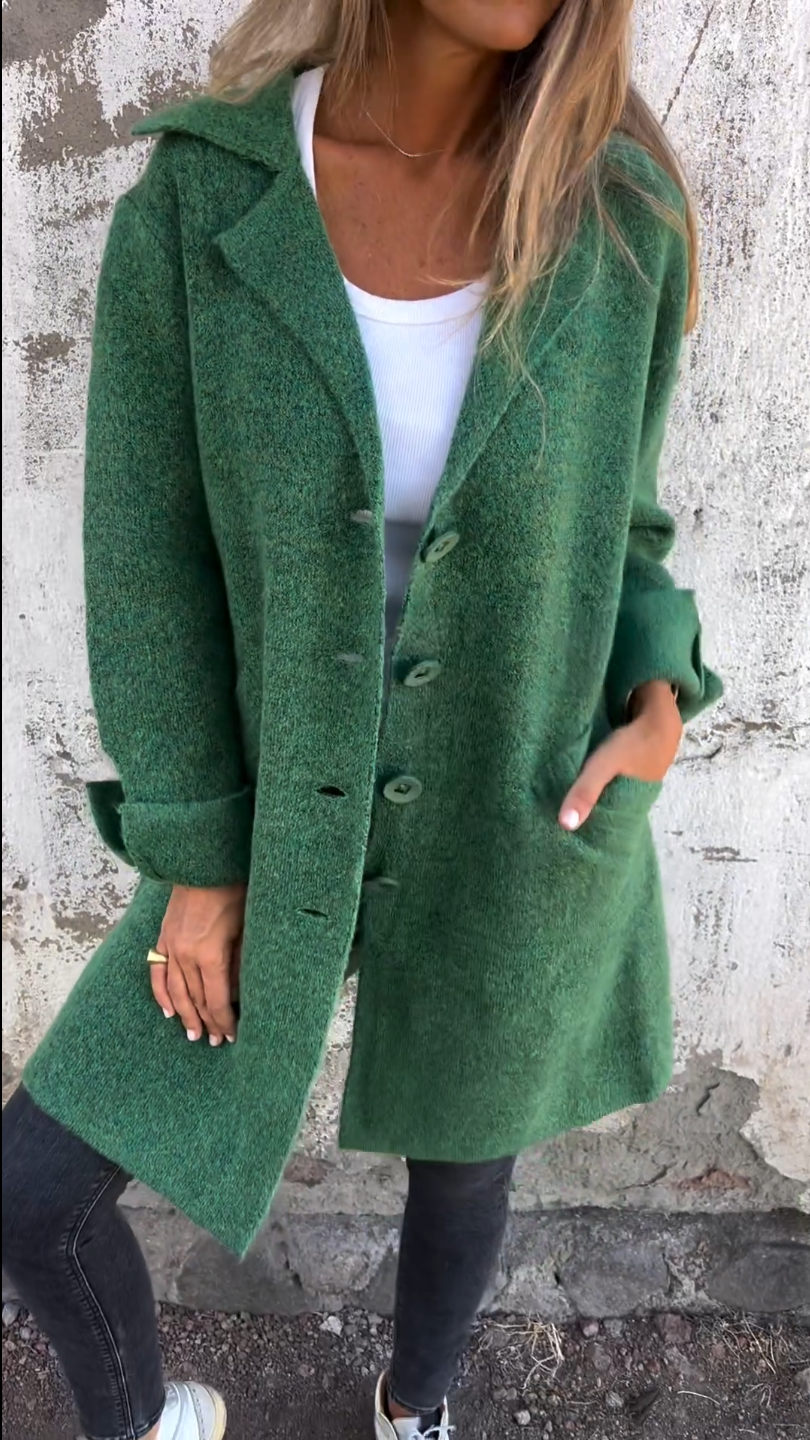 Femme portant un manteau vert élégant, en laine, avec boutons, sur fond de mur texturé. Mode automne, style décontracté, tendance vestimentaire.