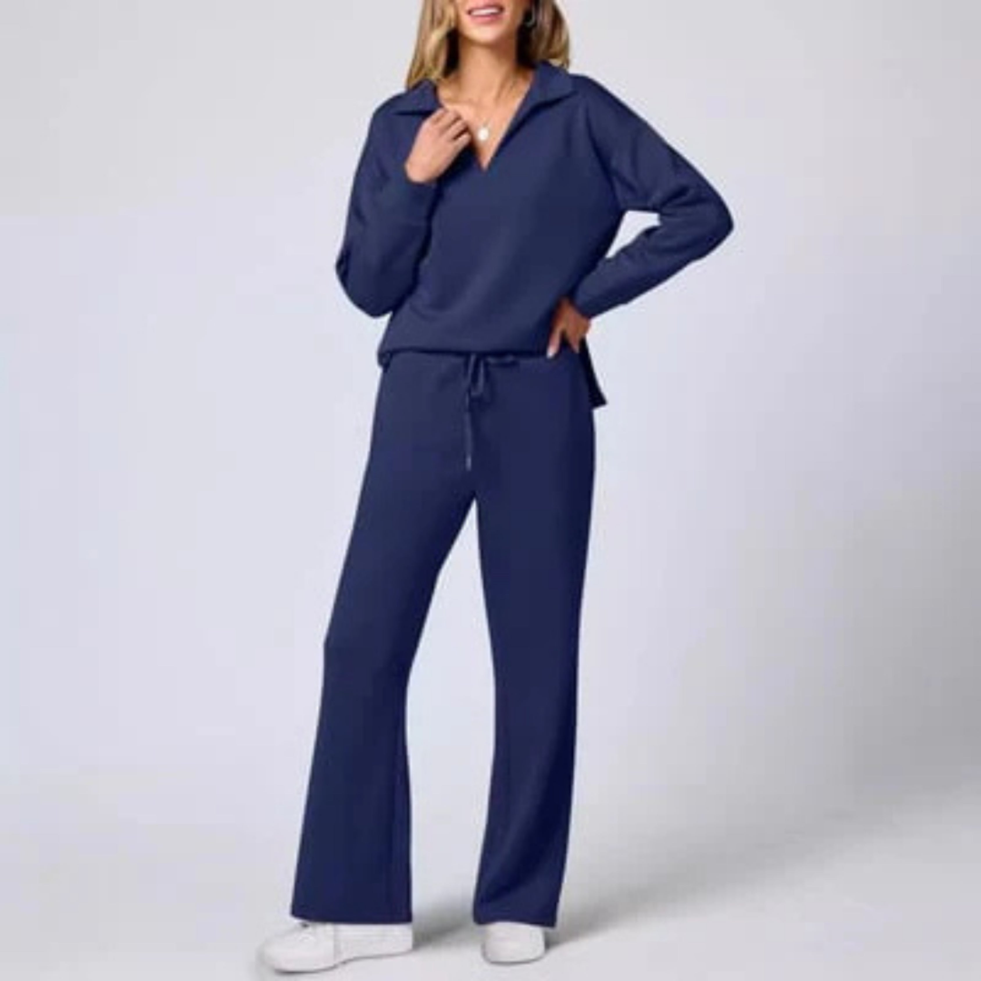Femme portant un ensemble décontracté bleu marine, composé d'un pull à col ouvert et d'un pantalon ample, avec des baskets blanches. Mode confortable.