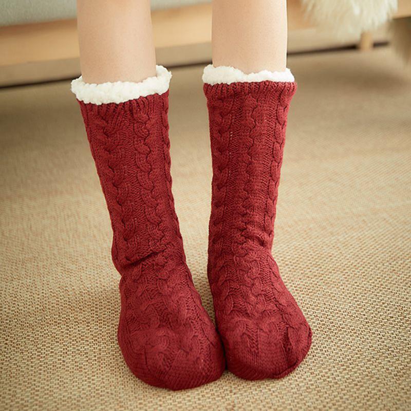 Chaussettes rouges en tricot torsadé avec doublure en laine blanche, posées sur un tapis beige. Accessoire d'hiver chaud et confortable.