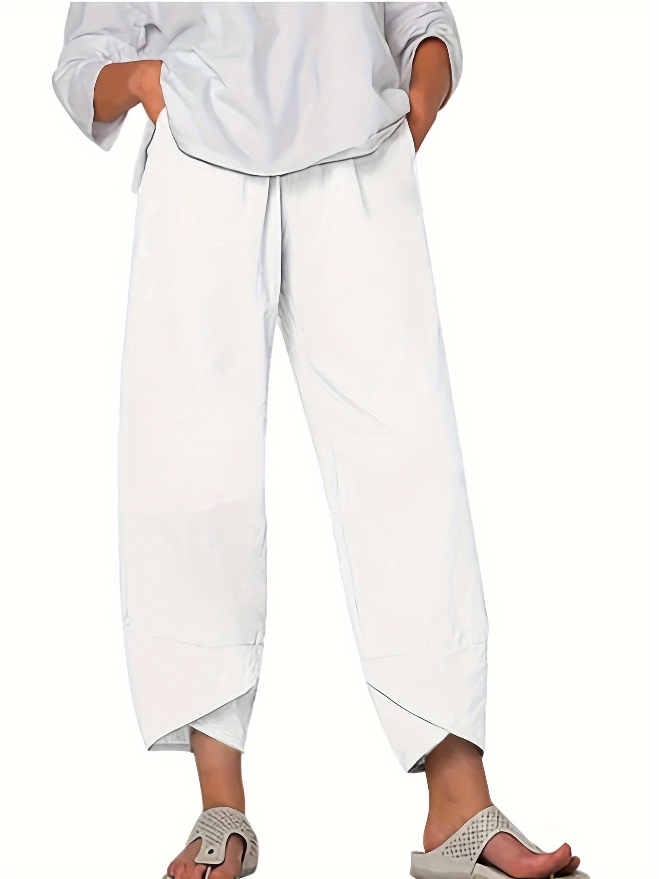 Pantalon blanc ample pour femme, style décontracté, avec ourlets asymétriques, associé à des sandales grises. Mode estivale élégante et confortable.