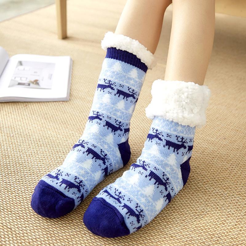 Chaussettes d'hiver bleues avec motifs de rennes et bordure en fourrure blanche, portées sur un tapis beige. Accessoire chaud et confortable.