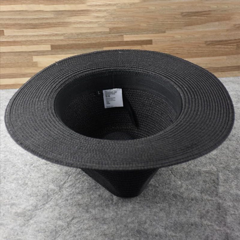 Chapeau noir en paille vu de dessus, posé sur un sol en bois et tapis gris. Accessoire de mode élégant, idéal pour l'été et les tenues décontractées.