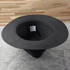 Chapeau noir en paille vu de dessus, posé sur un sol en bois et tapis gris. Accessoire de mode élégant, idéal pour l'été et les tenues décontractées.