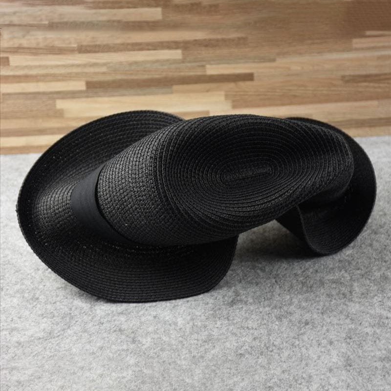 Chapeau noir en paille tressée, design sculptural, posé sur fond en bois et tapis gris. Accessoire de mode élégant et moderne.