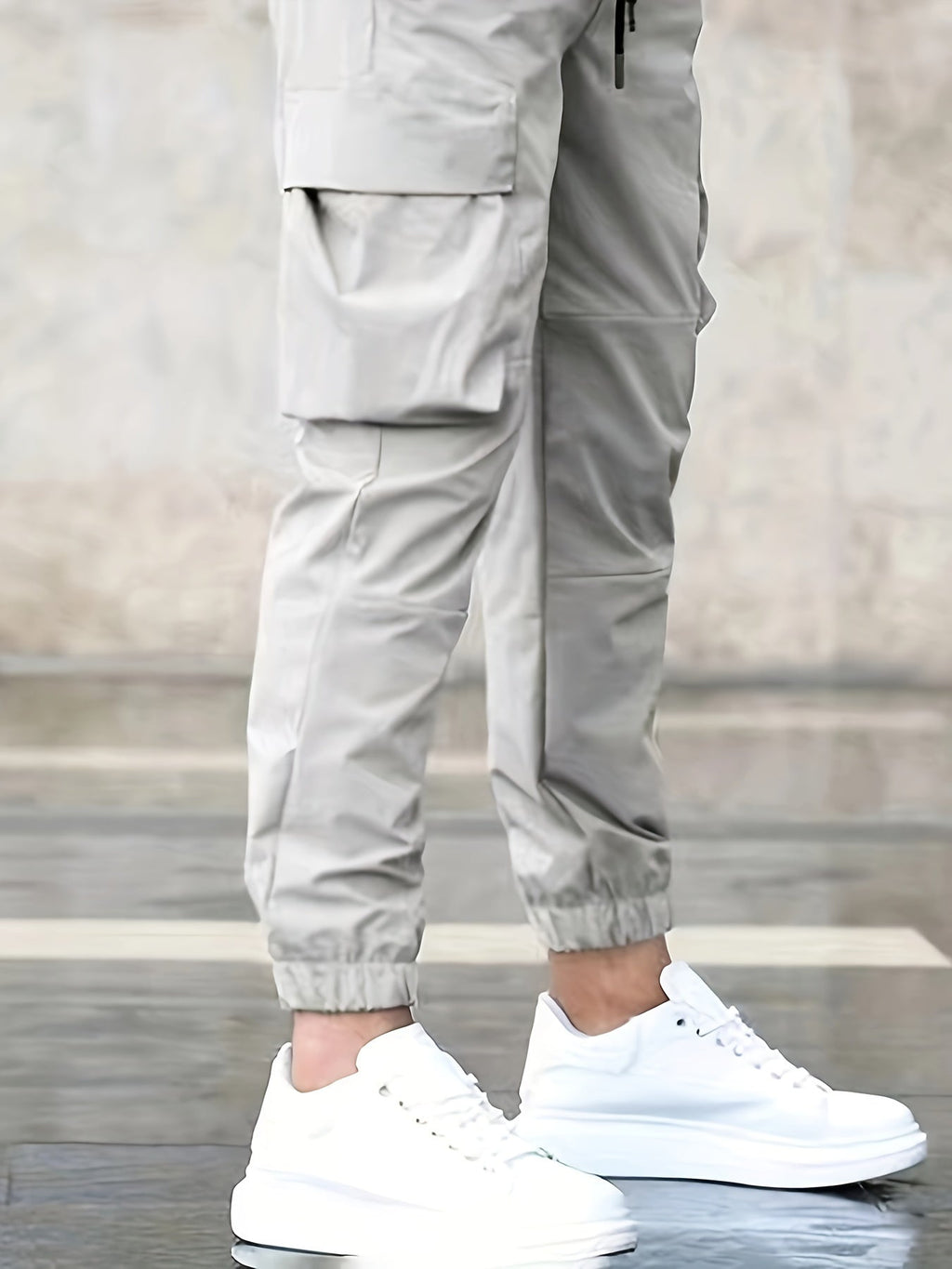 Pantalon cargo beige avec poches latérales, porté avec des baskets blanches sur un sol en pierre. Mode urbaine, style décontracté, tendance masculine.