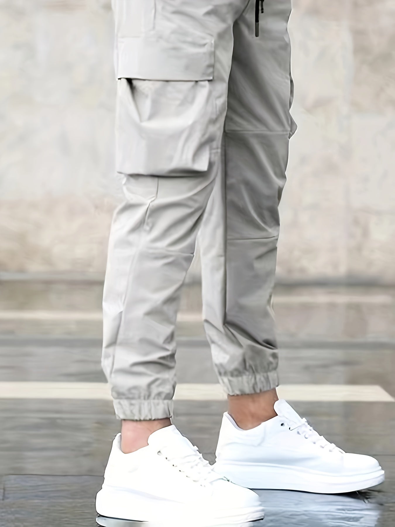 Pantalon cargo beige avec poches latérales, porté avec des baskets blanches sur un sol en pierre. Mode urbaine, style décontracté, tendance masculine.
