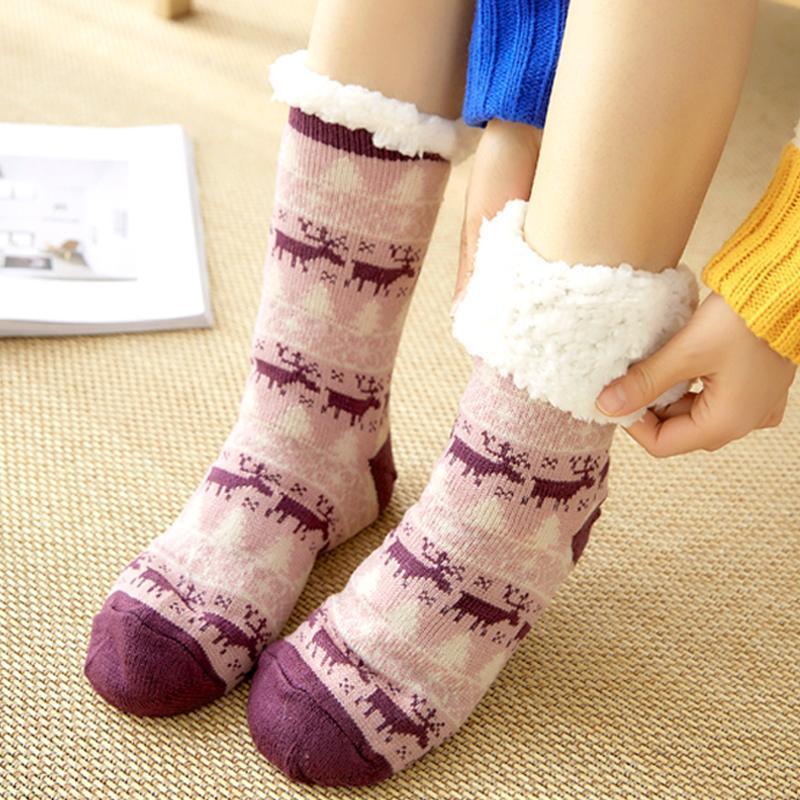 Chaussettes chaudes en laine rose avec motifs de rennes violets, portées sur un tapis beige. Accessoire d'hiver confortable et tendance.