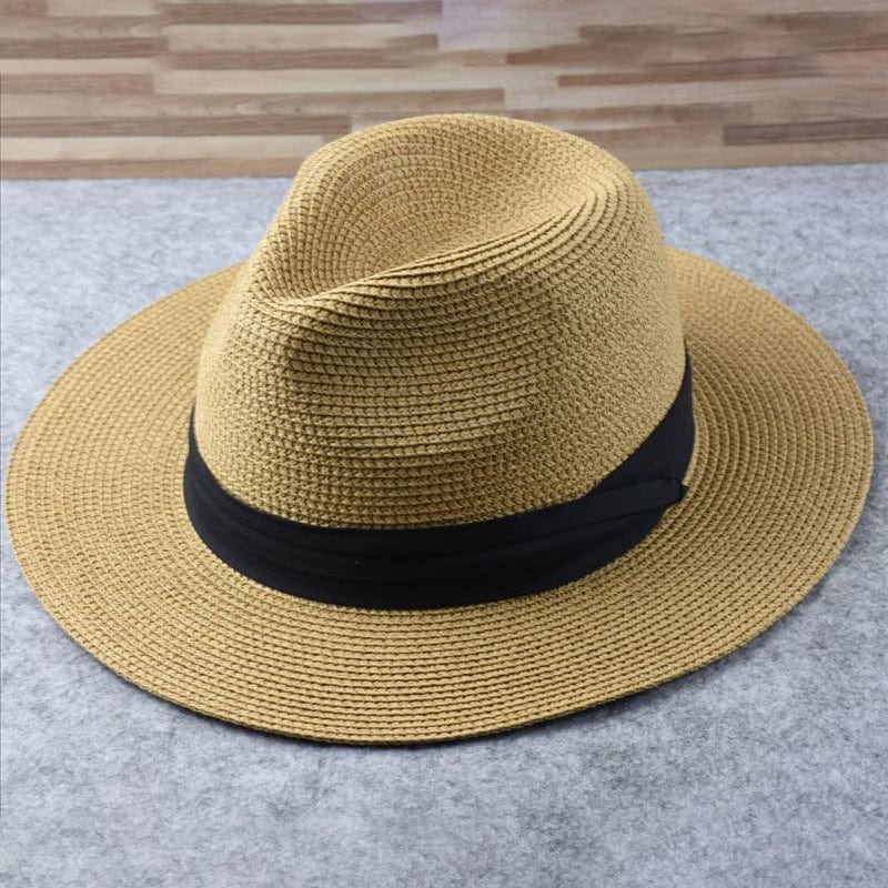 Chapeau Panama en paille beige avec ruban noir, posé sur une surface grise. Accessoire élégant, mode estivale, style classique.