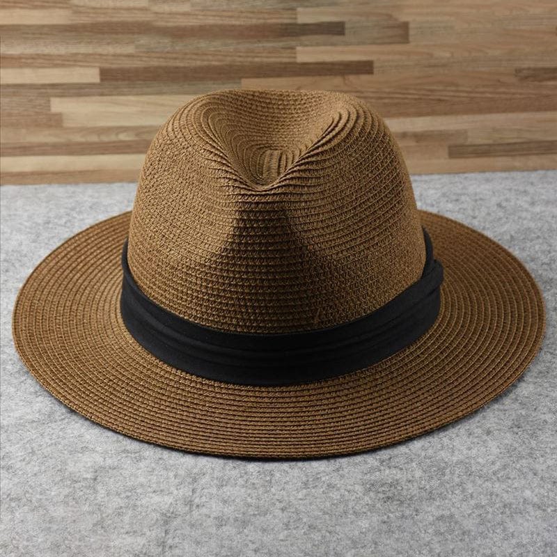 Chapeau Fedora en paille marron avec bande noire, posé sur une surface grise, fond en bois. Accessoire mode élégant, tendance été.