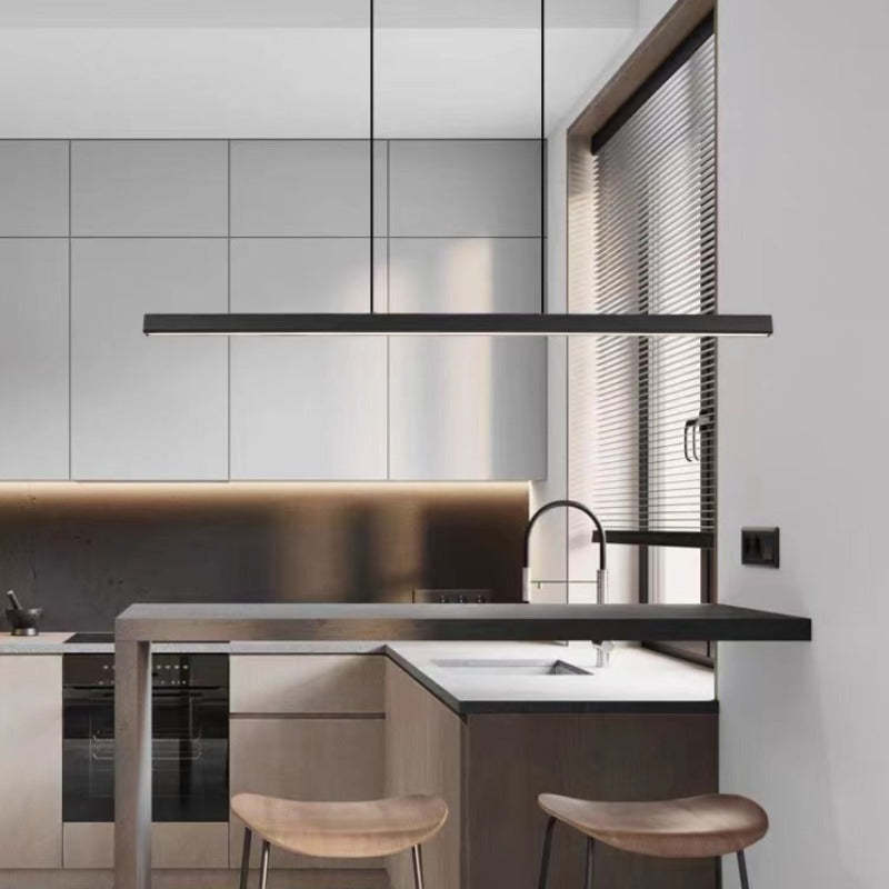 Cuisine moderne avec îlot central, tabourets en bois, éclairage suspendu, armoires grises, plan de travail blanc, et fenêtre avec stores vénitiens.