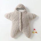 Combinaison bébé en forme d'étoile, en peluche beige, avec capuche. Idéale pour l'hiver, douce et chaude. Accessoire coloré à côté.