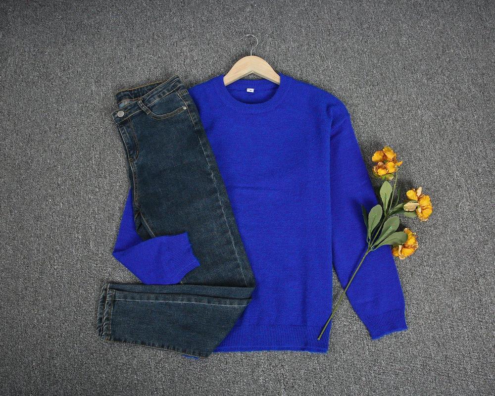 Pull bleu sur cintre avec jean bleu foncé et fleurs jaunes sur fond gris. Mode automne, vêtements décontractés, style tendance.