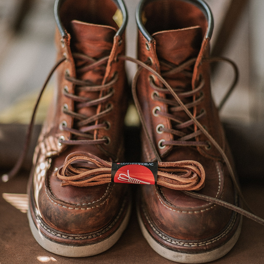 Bottes en cuir marron vintage avec lacets assortis, style robuste et durable, posées sur une surface en bois. Mode homme, chaussures de travail.