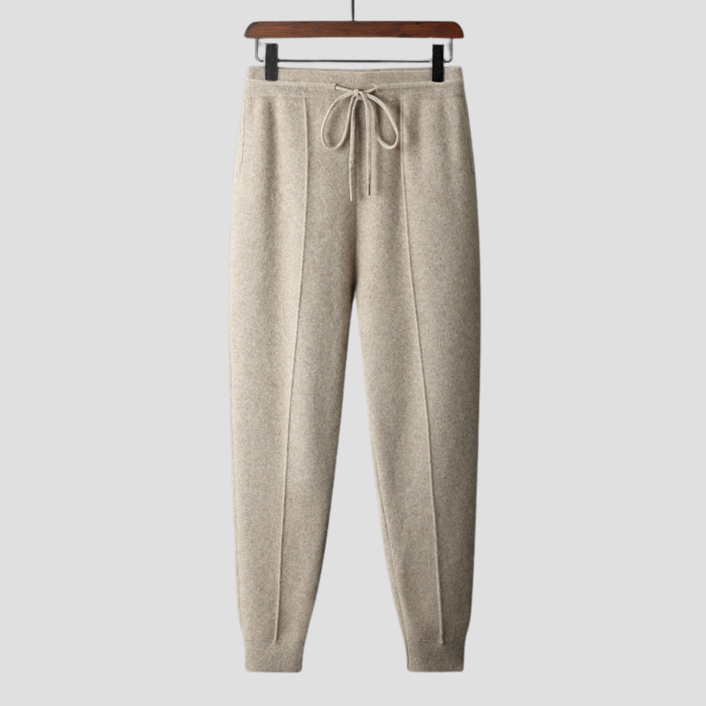 Pantalon de jogging beige en laine, suspendu sur un cintre en bois, avec cordon de serrage. Mode décontractée, vêtements confortables, tendance automne.