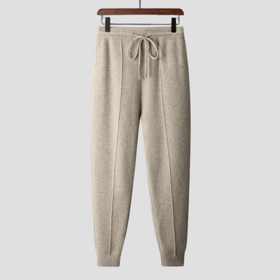 Pantalon de jogging beige en laine, suspendu sur un cintre en bois, avec cordon de serrage. Mode décontractée, vêtements confortables, tendance automne.