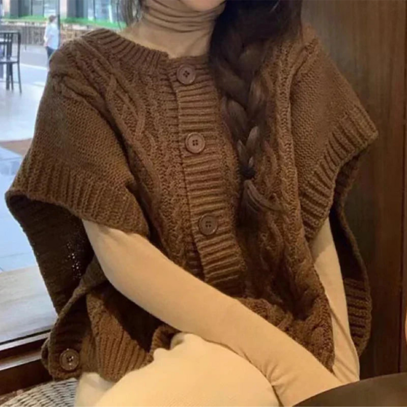 Femme portant un poncho en tricot marron avec boutons, col roulé beige, assise dans un café. Mode automne-hiver, style décontracté et élégant.