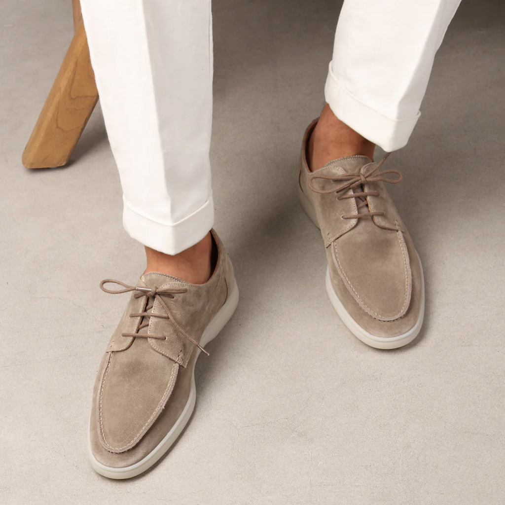 Chaussures derby en daim beige pour homme, élégantes et modernes, portées avec un pantalon blanc. Mode masculine, style décontracté chic.