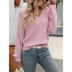 Femme portant un pull rose en tricot avec manches ajourées, jeans bleu clair et ceinture blanche. Mode féminine décontractée, tendance automne.