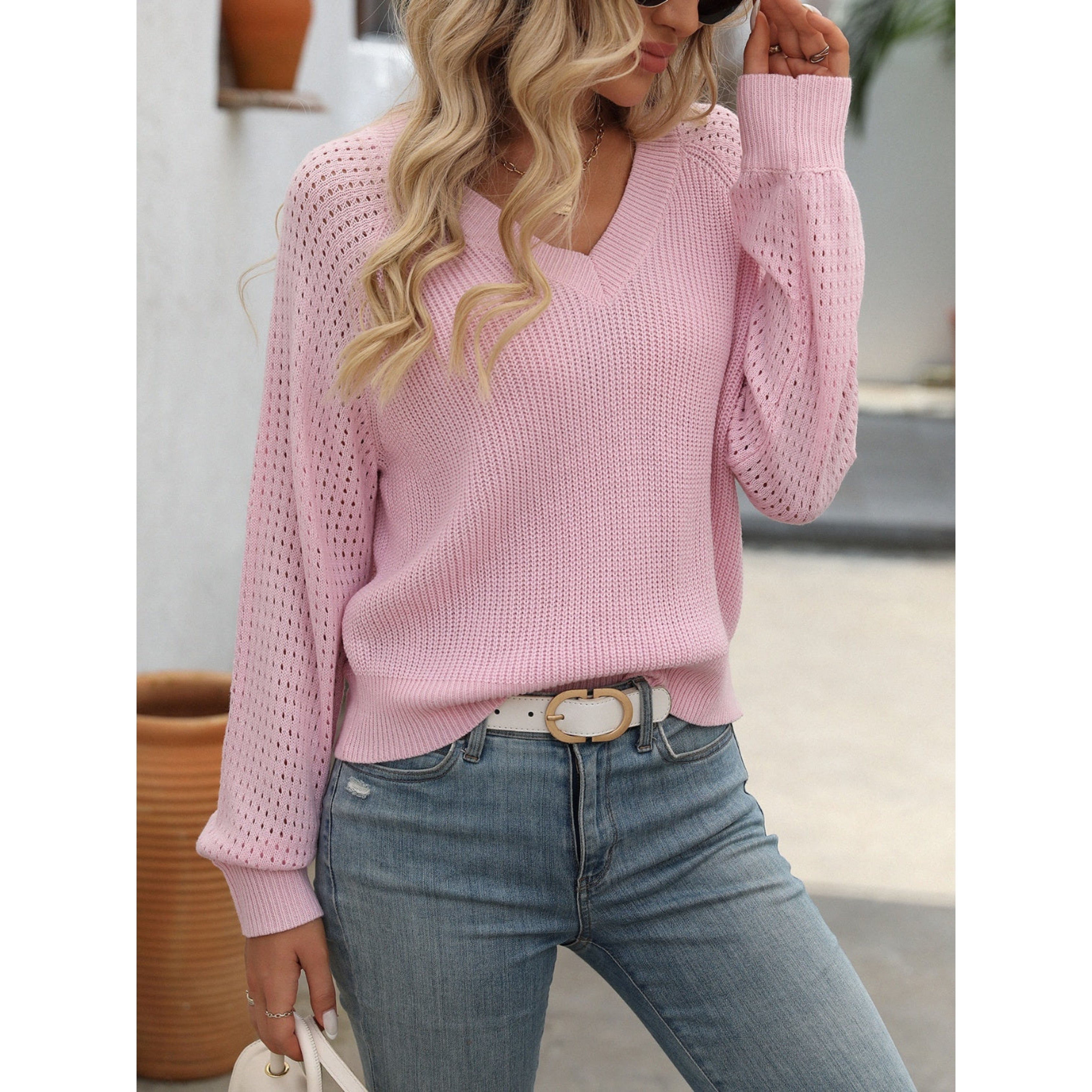 Femme portant un pull rose en tricot avec manches ajourées, jeans bleu clair et ceinture blanche. Mode féminine décontractée, tendance automne.
