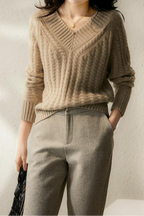 Femme portant un pull en maille beige avec un motif torsadé, associé à un pantalon gris élégant. Mode automne-hiver, style chic et décontracté.