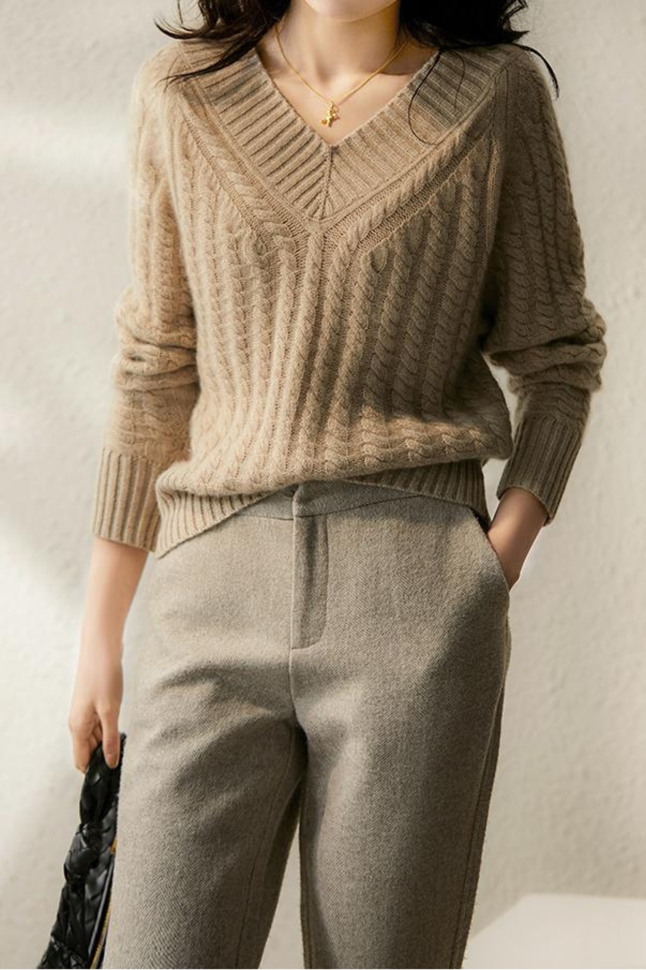 Femme portant un pull en maille beige avec un motif torsadé, associé à un pantalon gris élégant. Mode automne-hiver, style chic et décontracté.