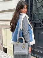 Femme portant un sac à main Dior gris, posant en manteau en jean doublé de fourrure, devant une porte noire. Mode urbaine élégante et tendance.