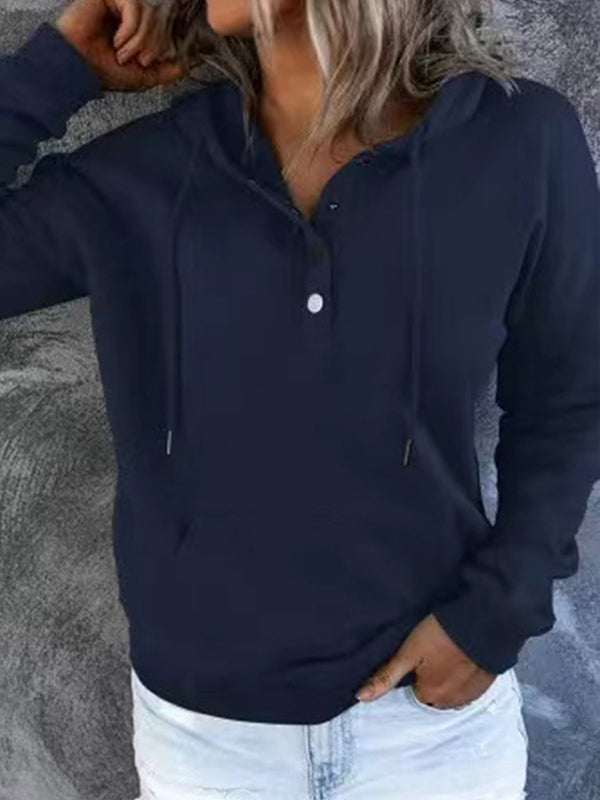 Femme portant un sweat à capuche bleu marine avec boutons, manches longues, et cordons, posant devant un fond gris. Mode décontractée, tendance automne.