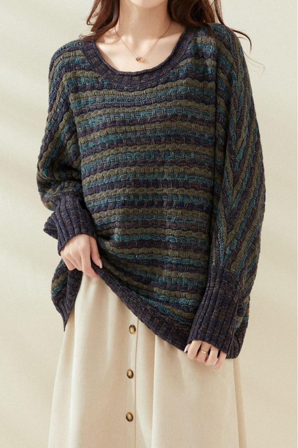 Femme portant un pull rayé bleu et vert, manches longues, avec une jupe beige à boutons. Mode automne-hiver, style décontracté et élégant.