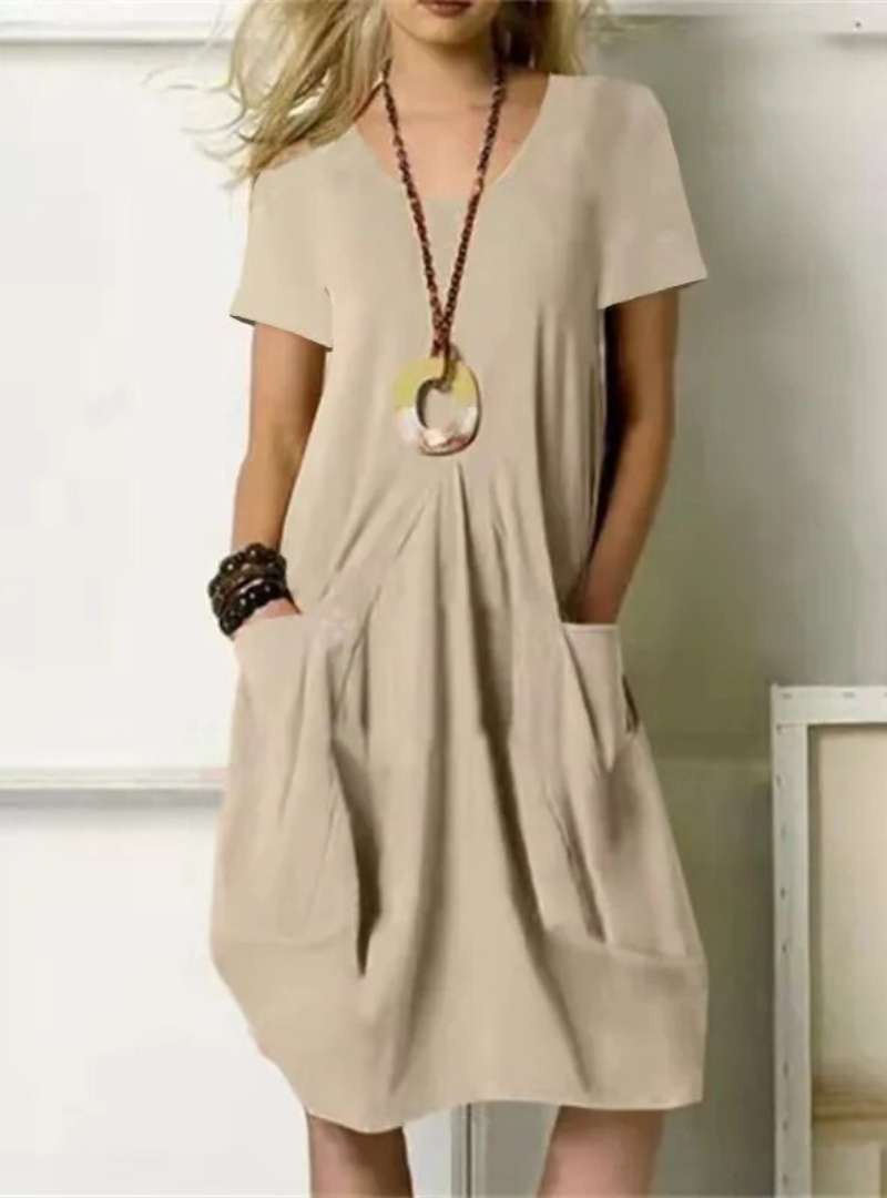 Robe beige ample avec poches, collier pendentif rond, portée par une femme. Mode décontractée, style estival, tenue élégante et confortable.