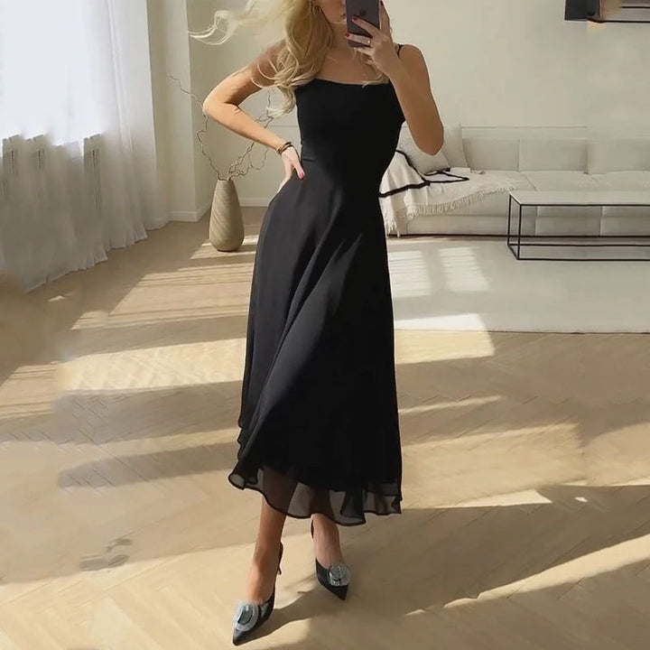 Robe noire élégante portée par une femme dans un salon moderne, lumière naturelle, parquet clair, ambiance chic et minimaliste.