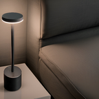 Lampe de chevet moderne noire sur table blanche, éclairant un canapé gris. Design minimaliste, éclairage d'ambiance, décoration intérieure élégante.