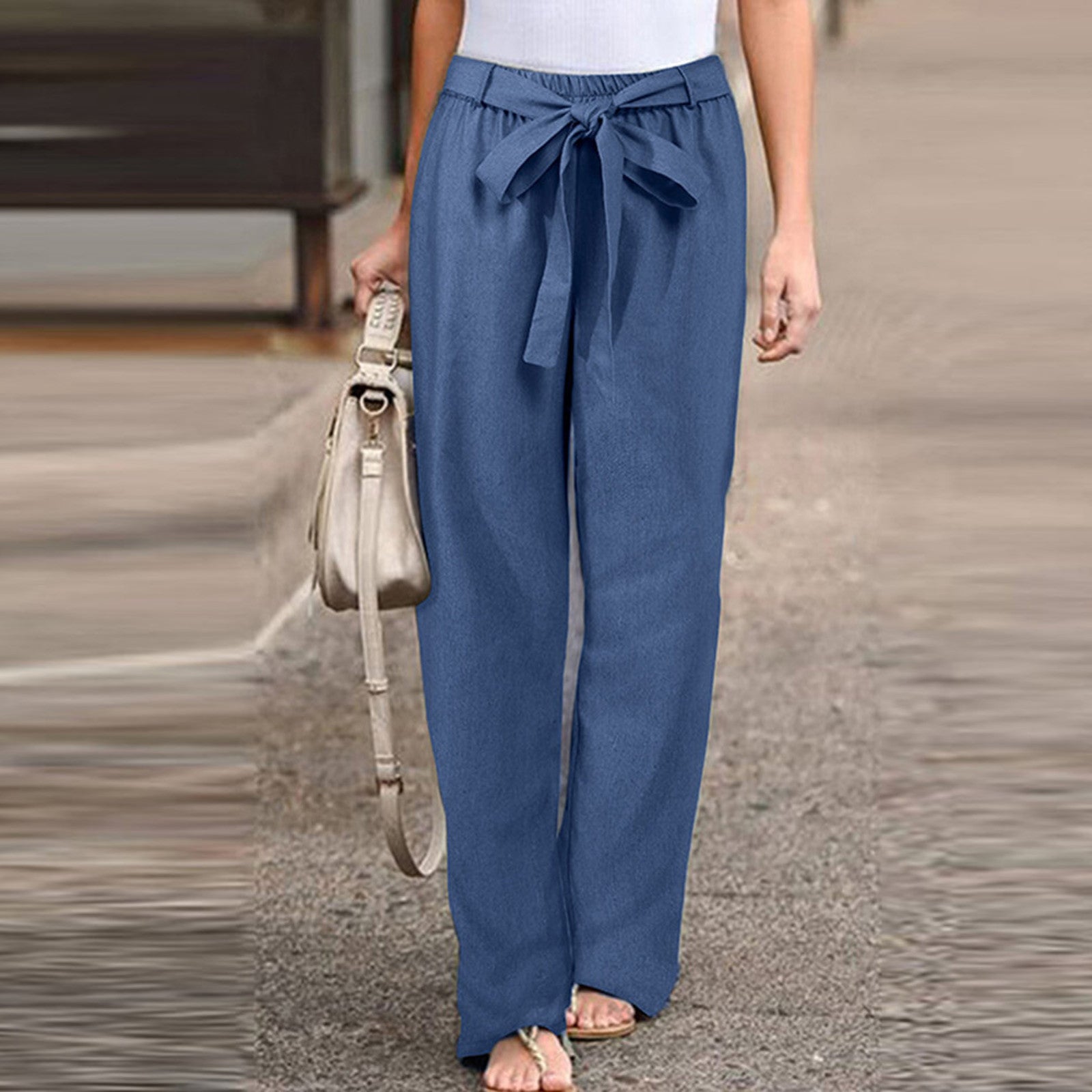 Pantalon large bleu avec ceinture nouée, porté par une femme, accompagné d'un sac à main beige. Mode décontractée, tendance estivale.