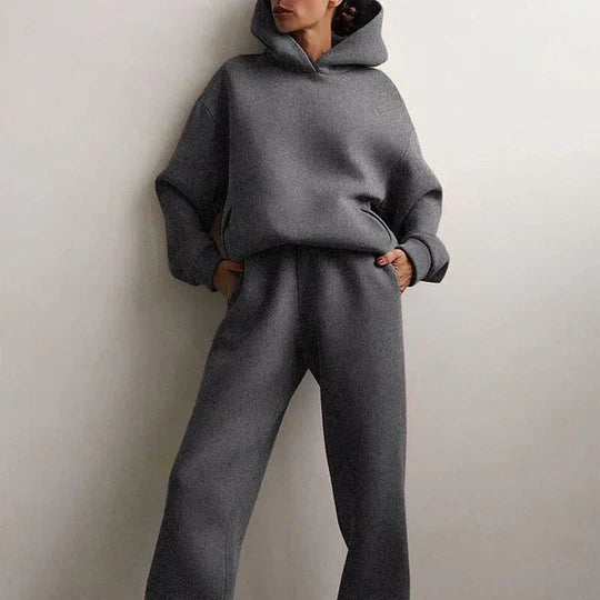 Femme portant un ensemble survêtement gris, composé d'un sweat à capuche et d'un pantalon ample. Mode décontractée, tendance automne-hiver.