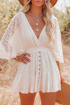 Robe blanche en dentelle avec manches évasées, portée par une femme blonde dans un champ. Mode estivale, style bohème chic, accessoires dorés.