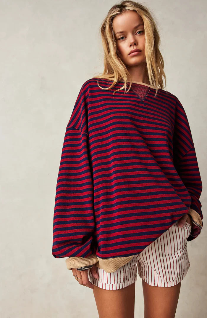Femme portant un pull rayé rouge et bleu surdimensionné, manches retroussées, avec un short rayé blanc et rouge. Mode décontractée, tendance automne.