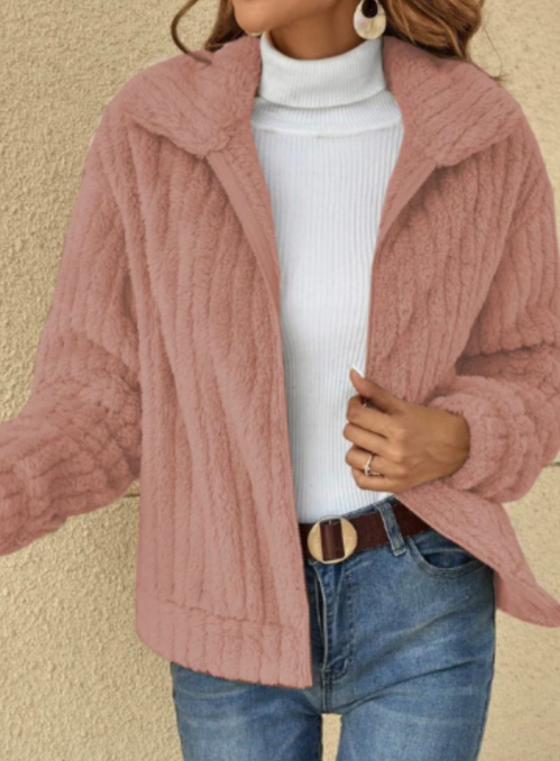 Veste en fausse fourrure rose, portée sur un pull blanc à col roulé, avec jean bleu et ceinture marron. Mode automne-hiver élégante et tendance.