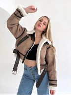 Jeune femme portant une veste aviateur marron avec doublure en fourrure blanche, posant avec un bras levé, sur fond blanc. Mode automne-hiver tendance.