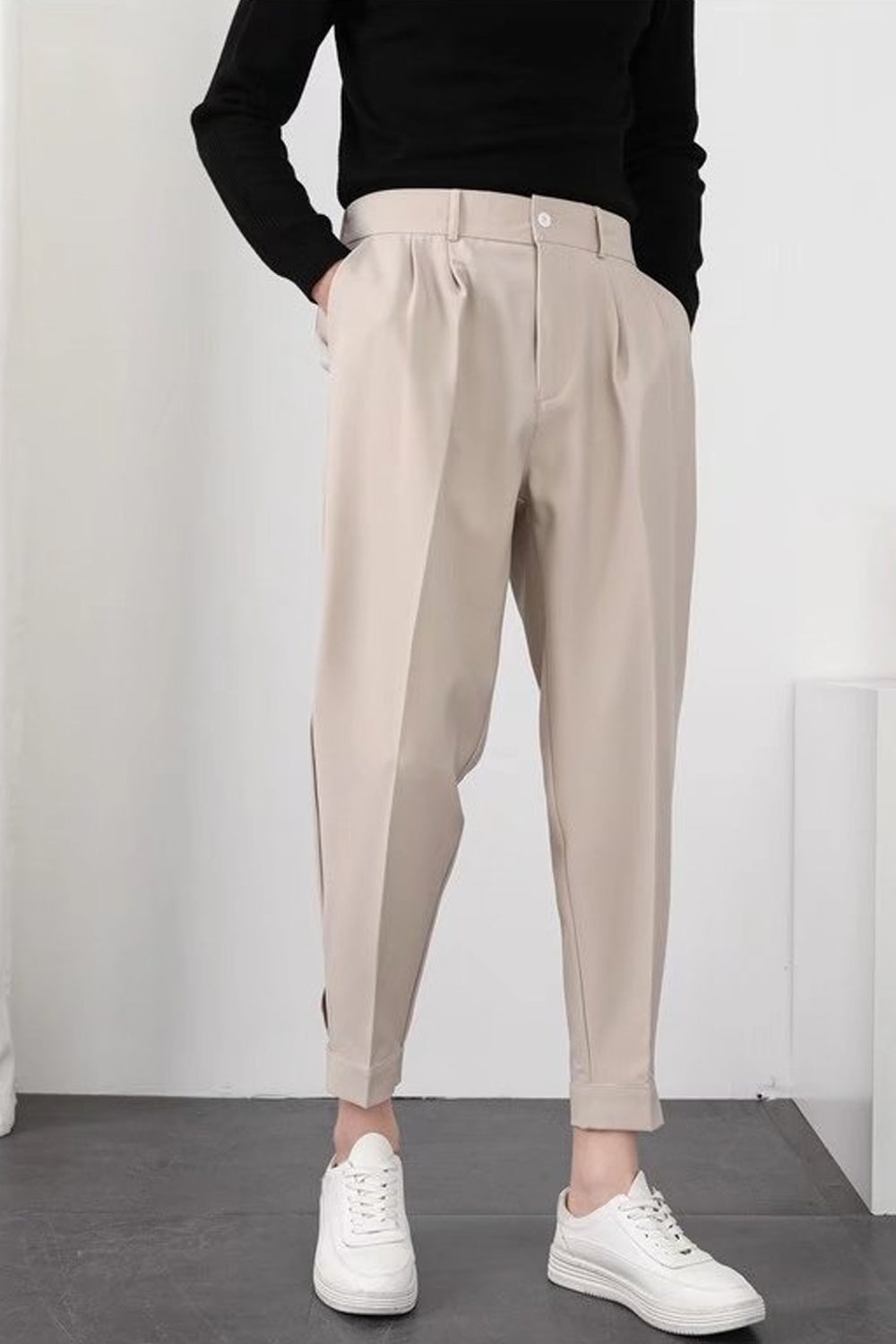 Pantalon beige ample pour femme, taille haute, avec pinces, porté avec un pull noir et des baskets blanches. Mode décontractée élégante.