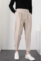 Pantalon beige ample pour femme, taille haute, avec pinces, porté avec un pull noir et des baskets blanches. Mode décontractée élégante.