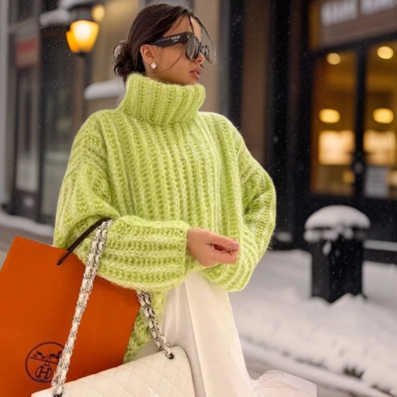 Femme en pull vert fluo, lunettes de soleil, sac blanc et sac orange, marchant dans une rue enneigée. Mode hiver, style urbain chic.