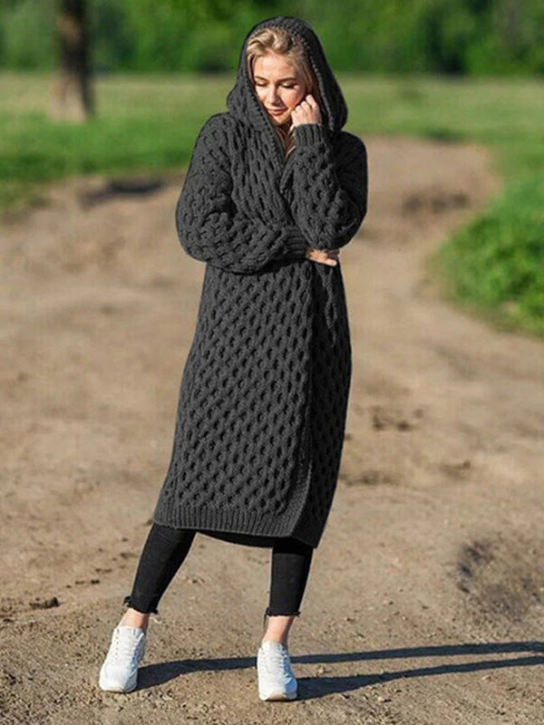 Femme portant un long cardigan à capuche en tricot gris, debout sur un chemin de terre, style décontracté, mode automne-hiver, confort et chaleur.