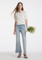 Femme portant un cardigan blanc texturé et un jean bleu clair, tenant un bouquet de fleurs. Mode élégante, style décontracté, tendance printemps.