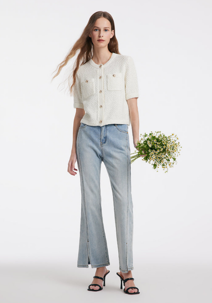 Femme portant un cardigan blanc texturé et un jean bleu clair, tenant un bouquet de fleurs. Mode élégante, style décontracté, tendance printemps.