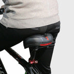 Homme en vélo avec selle ergonomique noire, coussin rembourré et lumière LED rouge. Confort cycliste, accessoires vélo, sécurité nocturne.