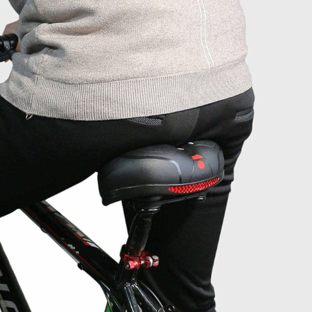 Homme en vélo avec selle ergonomique noire, coussin rembourré et lumière LED rouge. Confort cycliste, accessoires vélo, sécurité nocturne.